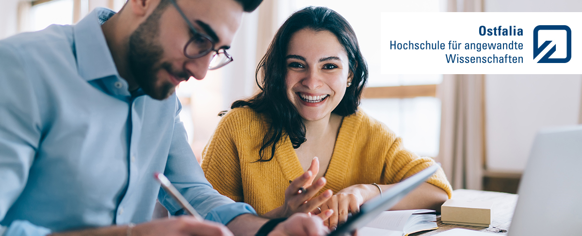 Pleased couple dressed in casual clothes writing notes in notebook while using tablet and sitting at table with laptop at home